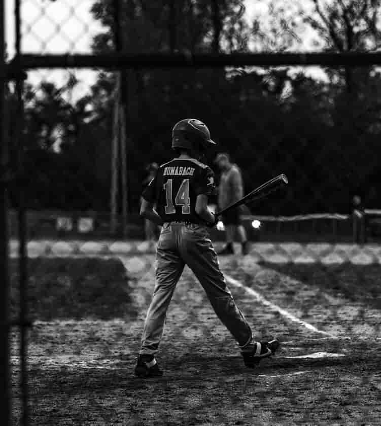 A young boy holding a baseball bat on a field, learning why it is called a shortstop in baseball.