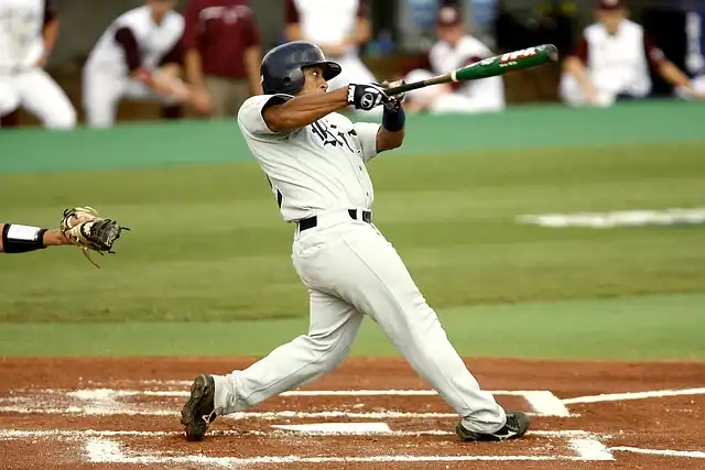 MLB Tryouts- The Full Guide to Tryouts for MLB and Independent Leagues 3 A baseball player in a grey uniform swings a bat at home plate during mlb tryouts, with a catcher poised to catch a pitch in the foreground.