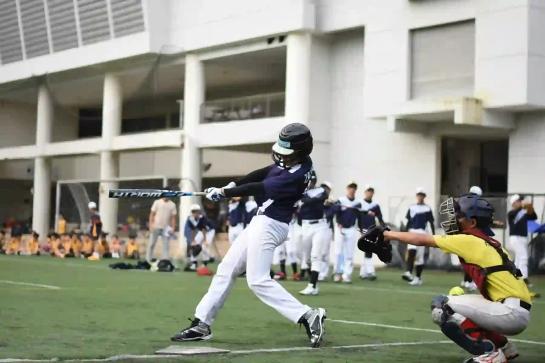 MLB Tryouts- The Full Guide to Tryouts for MLB and Independent Leagues 2 A young baseball player swings a bat during mlb tryouts, while a catcher prepares to receive the pitch in a lively sports environment.