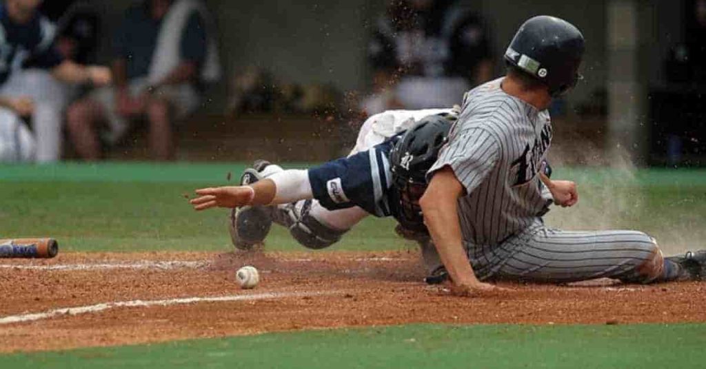 Home Team Advantage in Baseball: The World Series 2 A baseball player slides into home plate as a catcher attempts to tag him, with dirt flying in the air and a ball rolling nearby, illustrating the action near the area where does the home team sits in baseball.