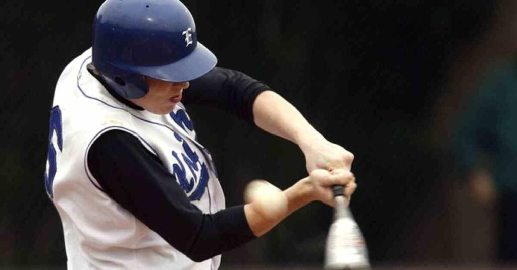 A baseball player mid-swing in a white uniform and blue helmet, releasing the bat in a bat drop motion as it begins to fall after the hit.