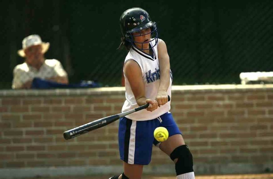 A young girl swinging a hot bat at a ball.