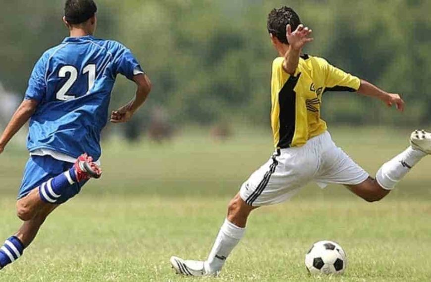 Two soccer players in action on the field, one in a blue jersey with number 21 and the other in yellow, showcasing athleticism that could lead to a discussion on how long is a football game.