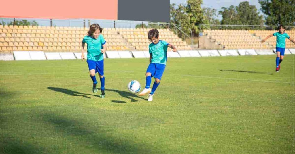 A group of young boys wearing football helmet stickers, kicking a soccer ball around on a field.