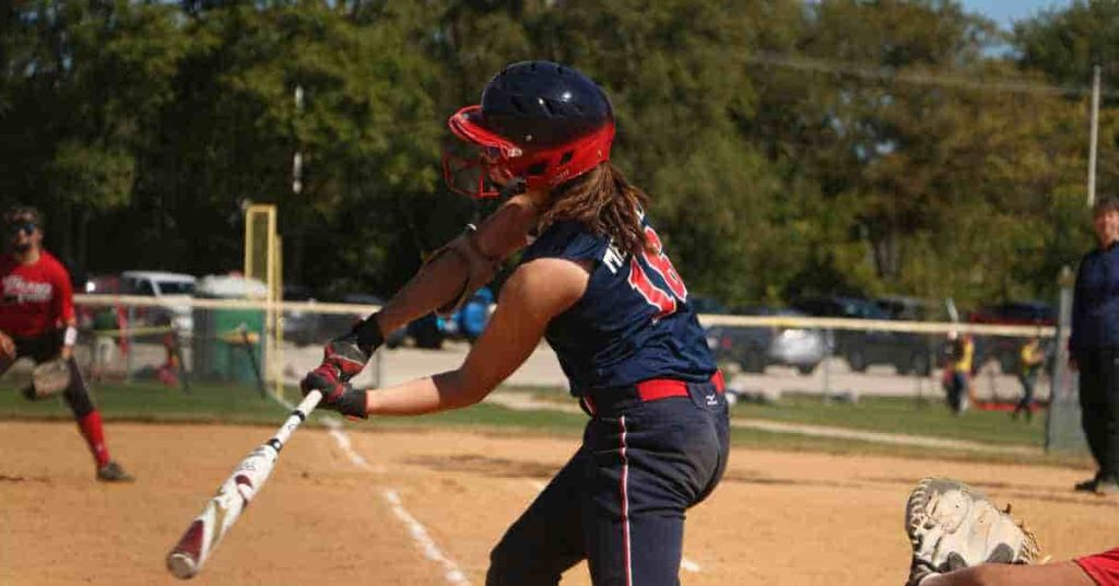 Bat Rolling.. What Is It, Benefits, Risks, and How It Works 2 A female softball player, using a bat rolling-enhanced bat, swings in preparation to hit a pitch, with teammates and spectators in the background.