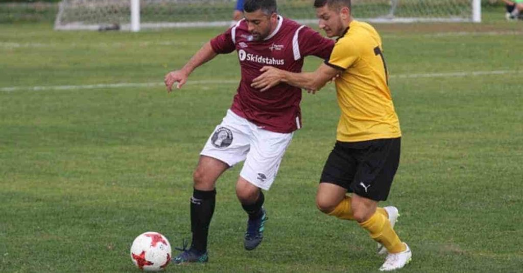 What does TBD in Football mean? How it’s used 2 Two soccer players compete for the ball on a green field, one in a maroon jersey and the other in a yellow uniform, illustrating a moment often labeled as tbd in football due to its uncertain outcome.