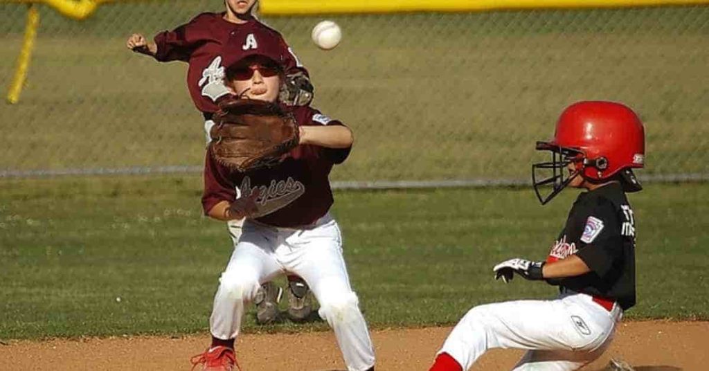 How Much Do Minor League Baseball Players Make?_ Salary Breakdown 2 A youth baseball game in action, illustrating the question 'how much do minor league baseball players make,' as a player in a black jersey slides into base while another attempts to throw the ball.