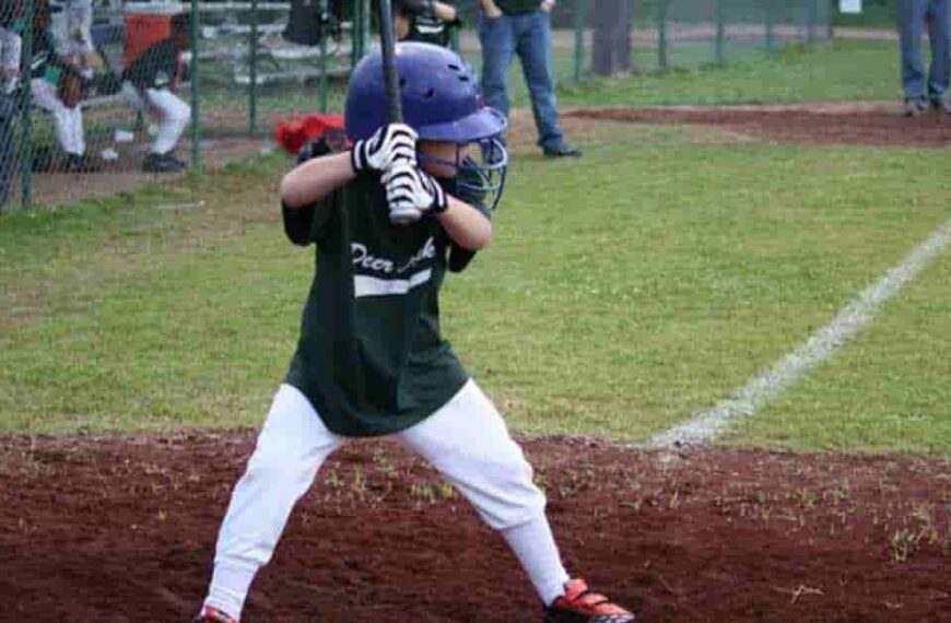 John Schneider coaching a young boy holding a baseball bat on a field.