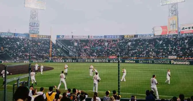 Baseball Positions by Number.. The Complete Guide 2 A crowded baseball stadium with players warming up on the field, illustrating Baseball Positions by Number, under a cloudy sky and bright stadium lights.