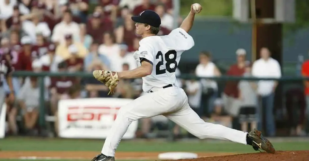 What Is Mercy Rule In Baseball-Understanding Baseball 4 A baseball pitcher in a white uniform winds up to throw a pitch, illustrating a moment before the mercy rule in baseball might come into effect, with a crowd of spectators in the background.