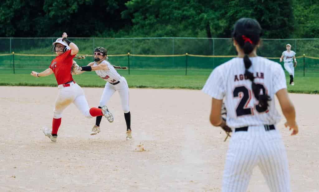Is Baseball a Contact Sport? Understanding the Nature of Baseball in the Sports World 3 Two softball players are in action on the field, one attempting a tag while another runs past, illustrating the dynamics of play when asking 'is baseball a contact sport.' A third player observes from a distance.